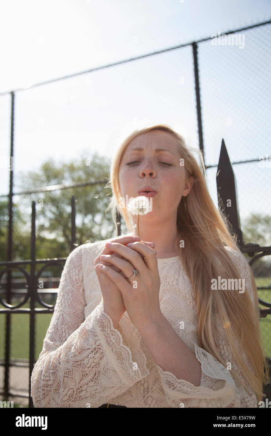 Jeune femme avec les yeux fermés blowing dandelion clock in park Banque D'Images