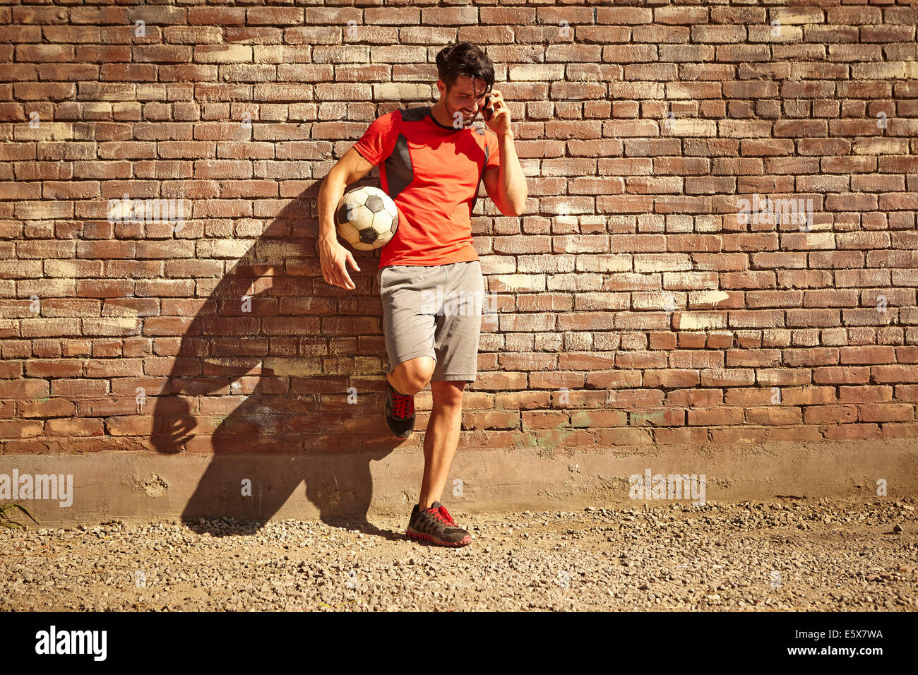 Young male soccer player chatting on smartphone sur wasteland Banque D'Images