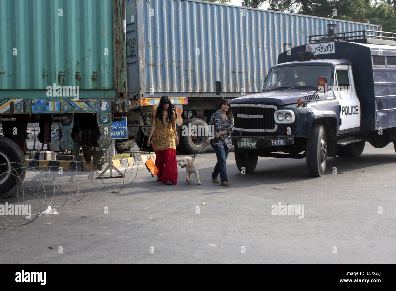 Lahore. 7e août, 2014. Les femmes pakistanaises traverser la route comme des conteneurs sont placés pour bloquer la zone près de la maison de l'érudit religieux Tahir-ul-Qadri avant de prochains rallye anti-gouvernement du Pakistan Tehreek Awami (PAT) dans l'est de Lahore au Pakistan le 7 août 2014. Tahir-ul-Qadri, a lancé la campagne contre Nawaz Sharif et a laissé entendre à rejoindre Khan en mars. La menace d'une manifestation nationale par le Tehrik-e-Insaf dirigé par cricketer-devenu politicien Imran Khan a mis la pression sur le gouvernement du Premier Ministre pakistanais Nawaz Sharif. © Jamil Ahmed/Xinhua/Alamy Live News Banque D'Images