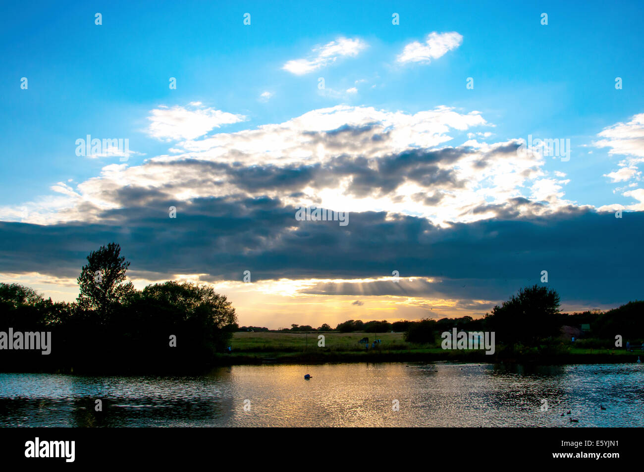 Nantwich lake juste avant le coucher du soleil avec le soleil qui brille à travers quelques nuages sombres Banque D'Images