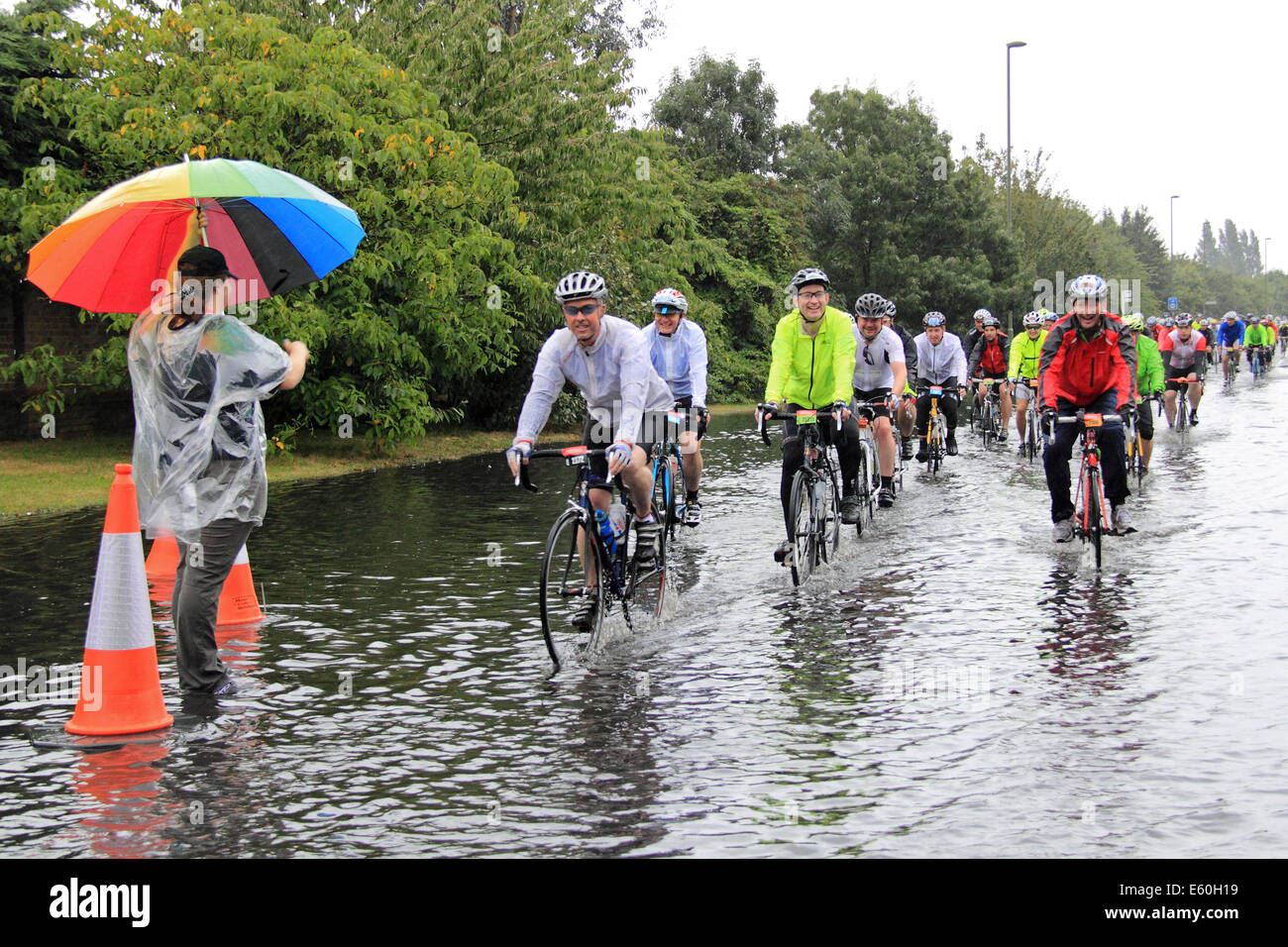 Dimanche 10 août 2014. Dunmurry, Surrey, UK. Les cyclistes la charrue par une route inondée après des pluies torrentielles ont occasionné par les restes de l'ouragan Bertha hits Prudential RideLondon-Surrey 100. 24 000 cyclistes amateurs ont pris part à l'événement qui s'étend sur 100 kilomètres et surtout suit l'itinéraire utilisé dans la course sur route olympique de Londres 2012. Cependant, en raison du mauvais temps, la route a été raccourcie à 86km). Crédit : Ian bouteille/Alamy Live News Banque D'Images