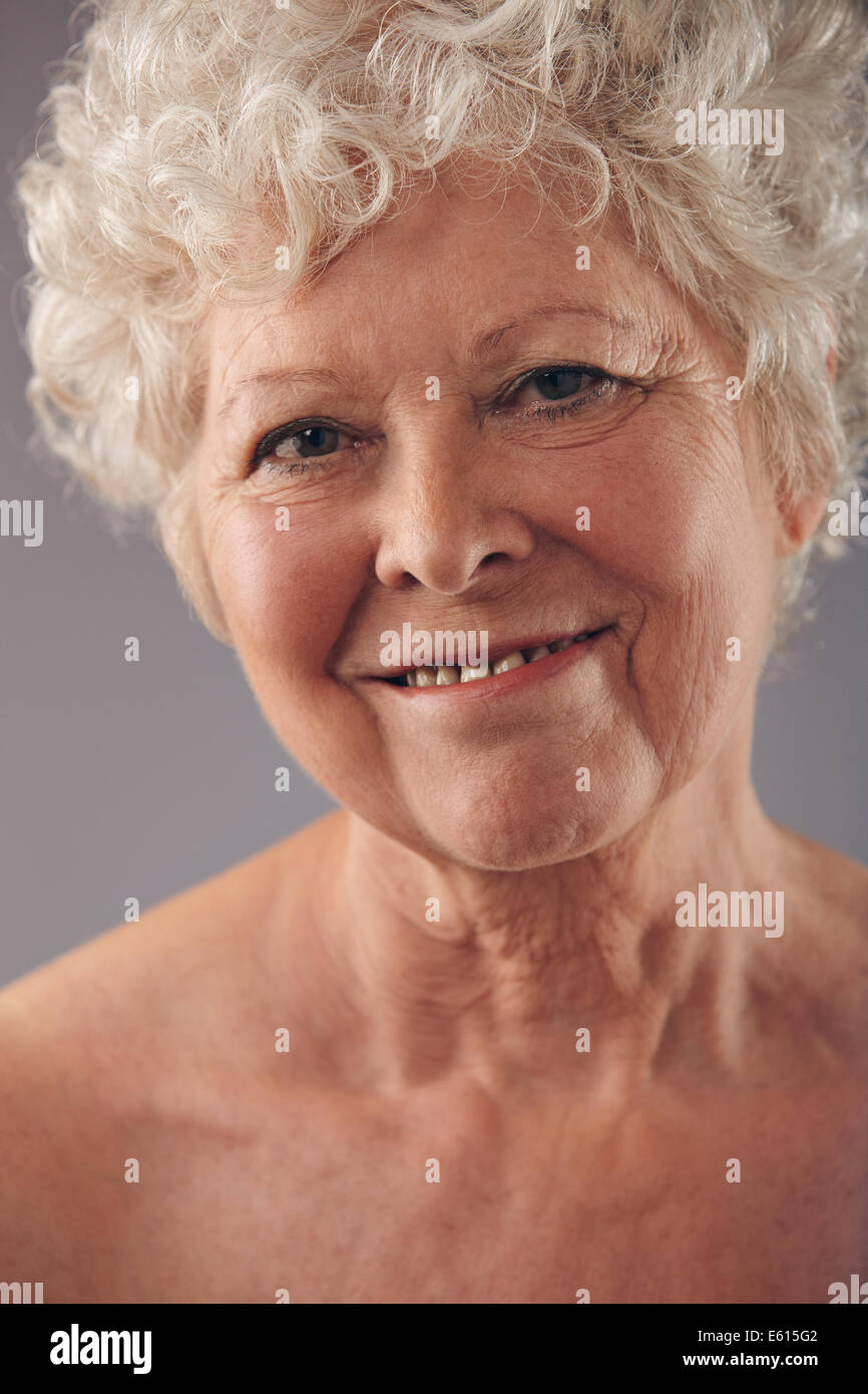 Portrait of attractive senior woman face avec un doux sourire contre fond gris. Femme mature positive. Banque D'Images