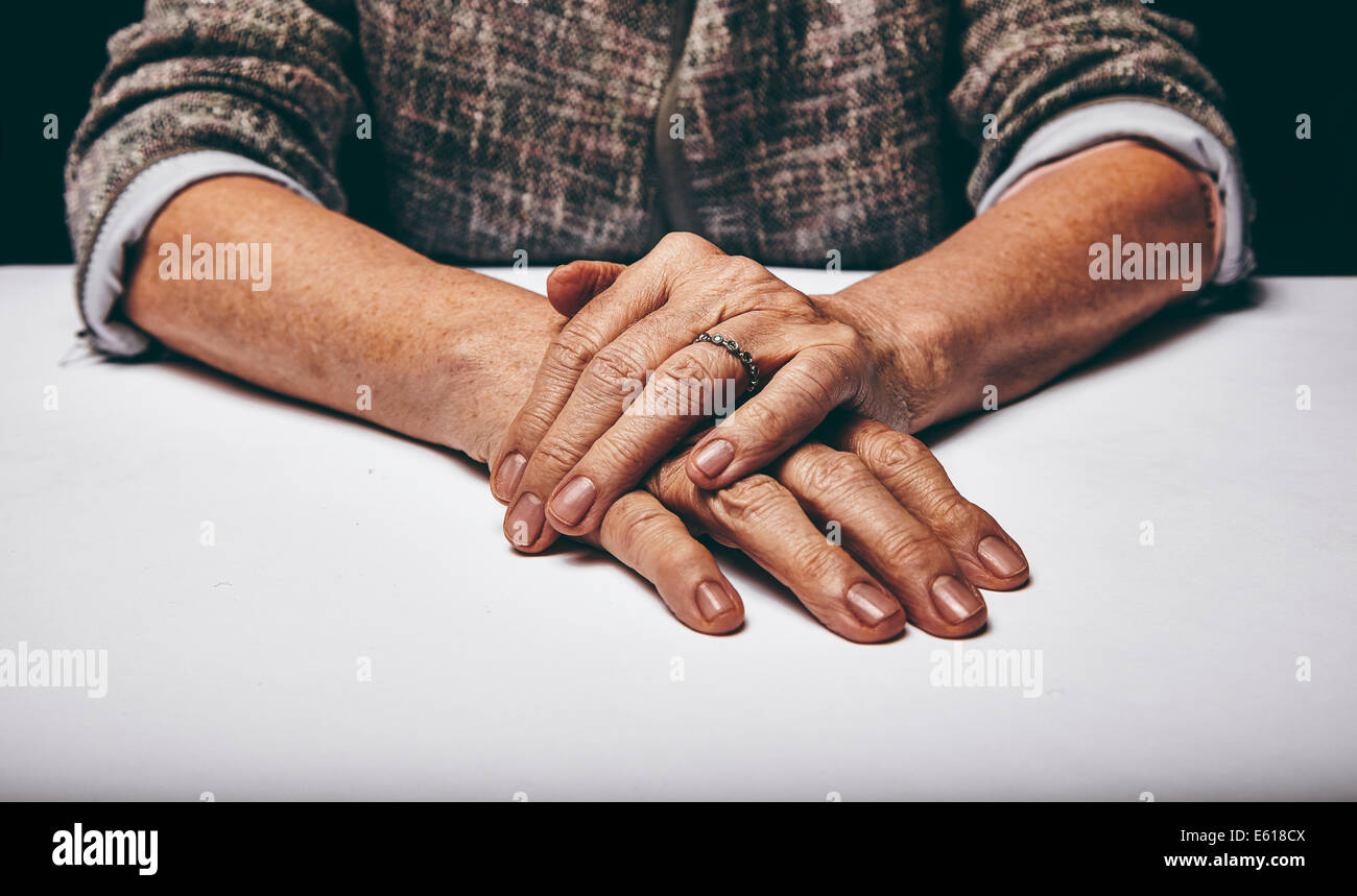 Studio shot of a senior woman's mains reposant sur la surface grise. Vieille dame assise avec elle les mains jointes sur une table. Banque D'Images
