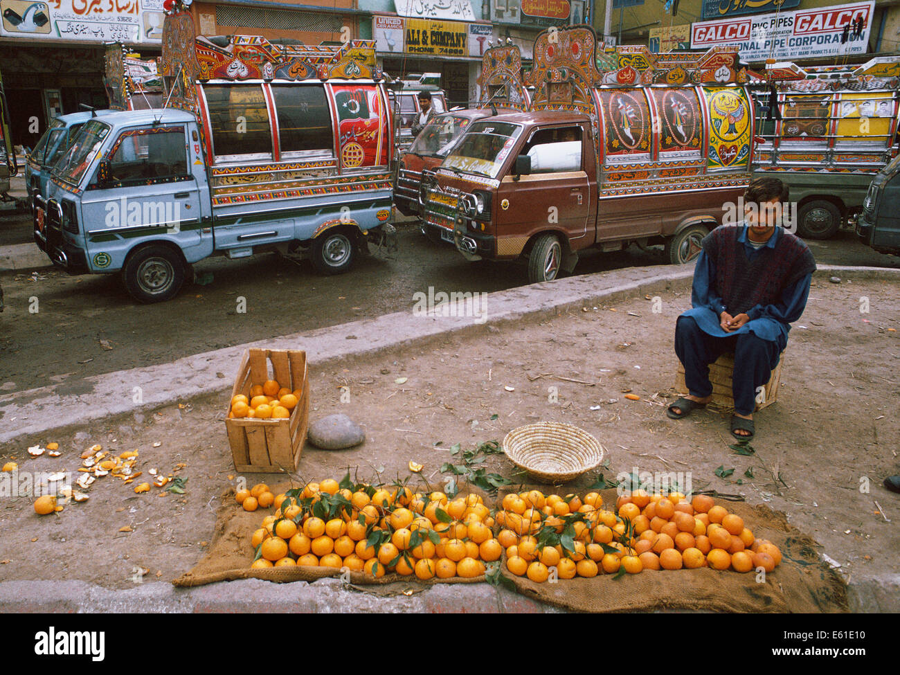Man selling oranges. Derrière lui, les mini-fourgonnettes sont en attente pour les passagers ( Pakistan) Banque D'Images