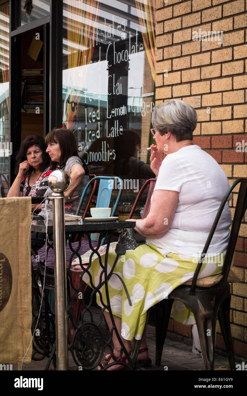 Senior, dame aux cheveux gris, assis dehors dans un café avec une tasse de café et de tabac. Banque D'Images