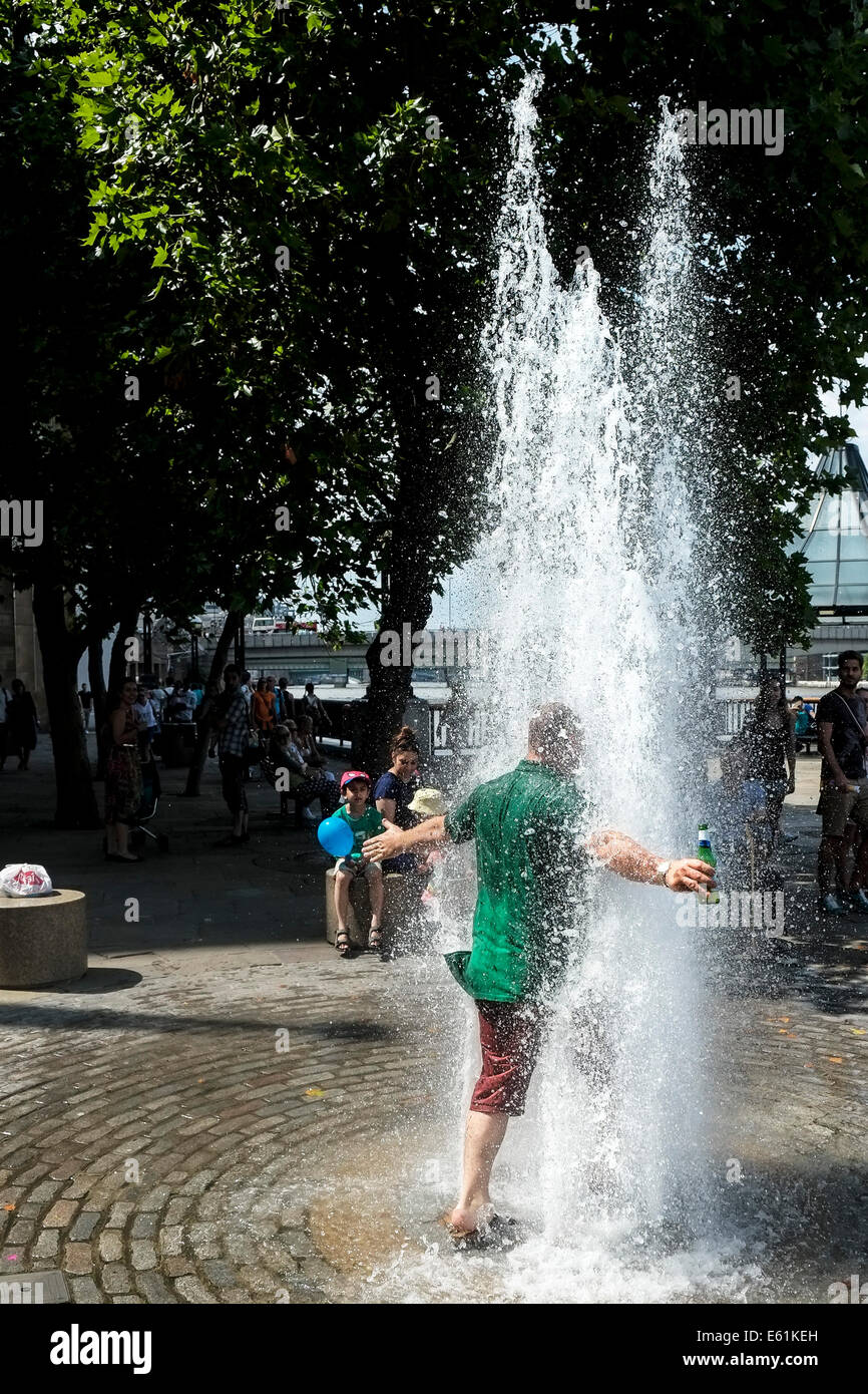 Un homme portant une bouteille de bière s'exécute dans une fontaine d'eau de s'échapper le temps chaud à Londres. Banque D'Images