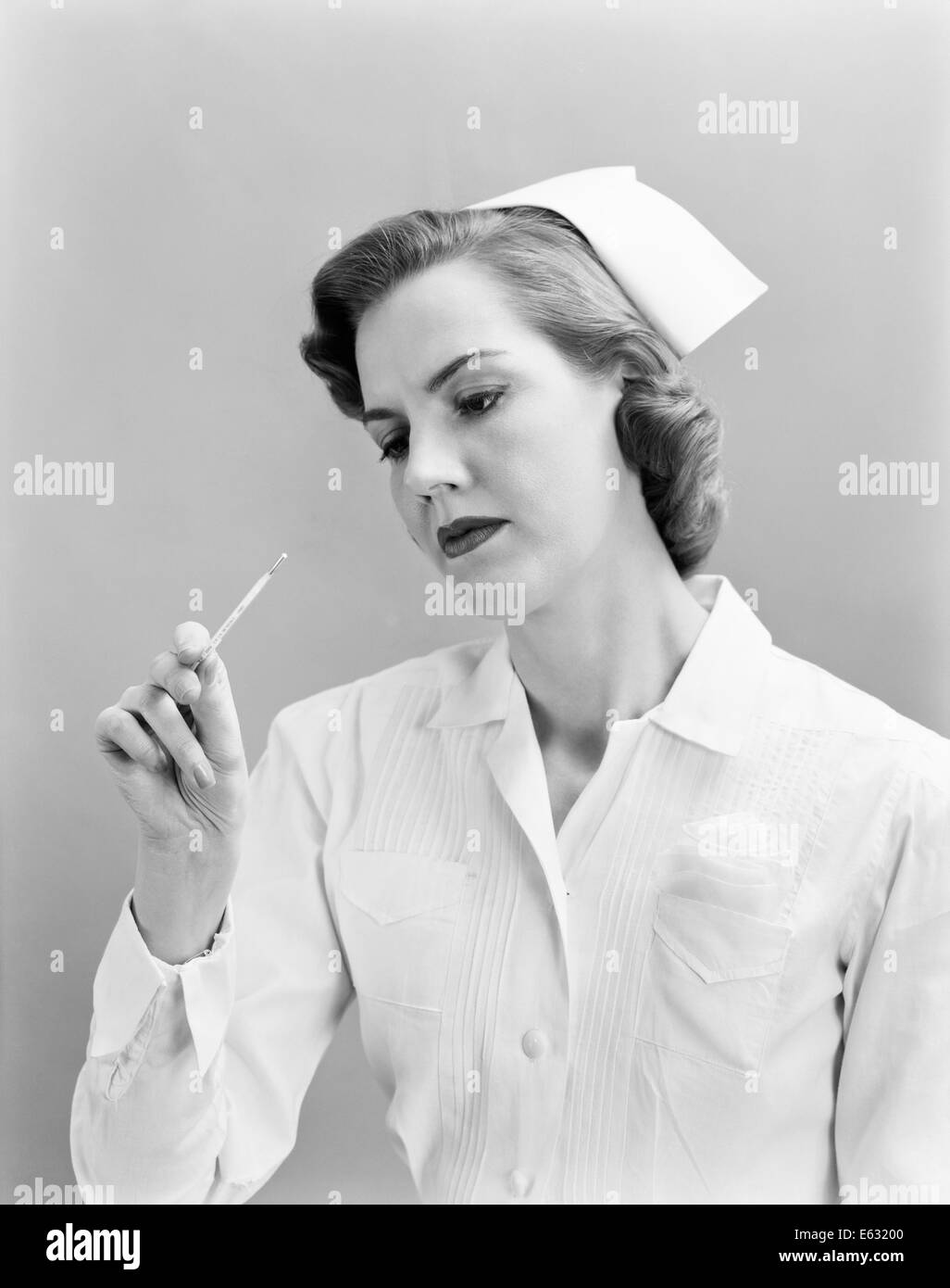 1950 FEMME INFIRMIÈRE CONTRÔLE LA TEMPÉRATURE SUR LE THERMOMÈTRE Banque D'Images