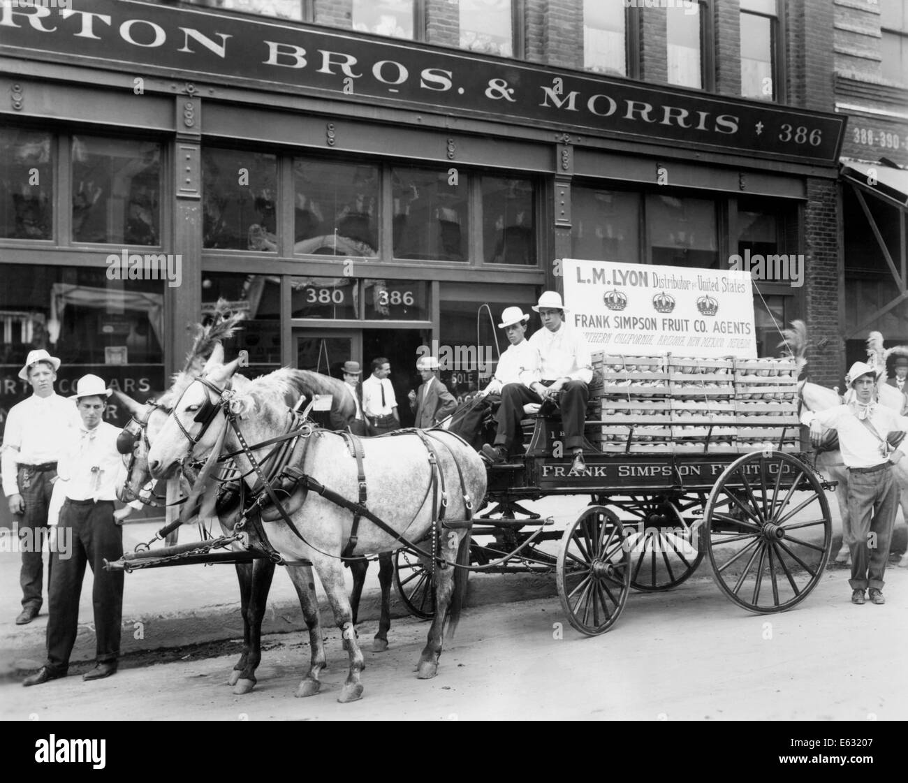 1890 MULE APPELÉE CHARIOT DE LIVRAISON DE FRUITS ON CITY STREET entouré d'HOMMES LOOKING AT CAMERA Banque D'Images