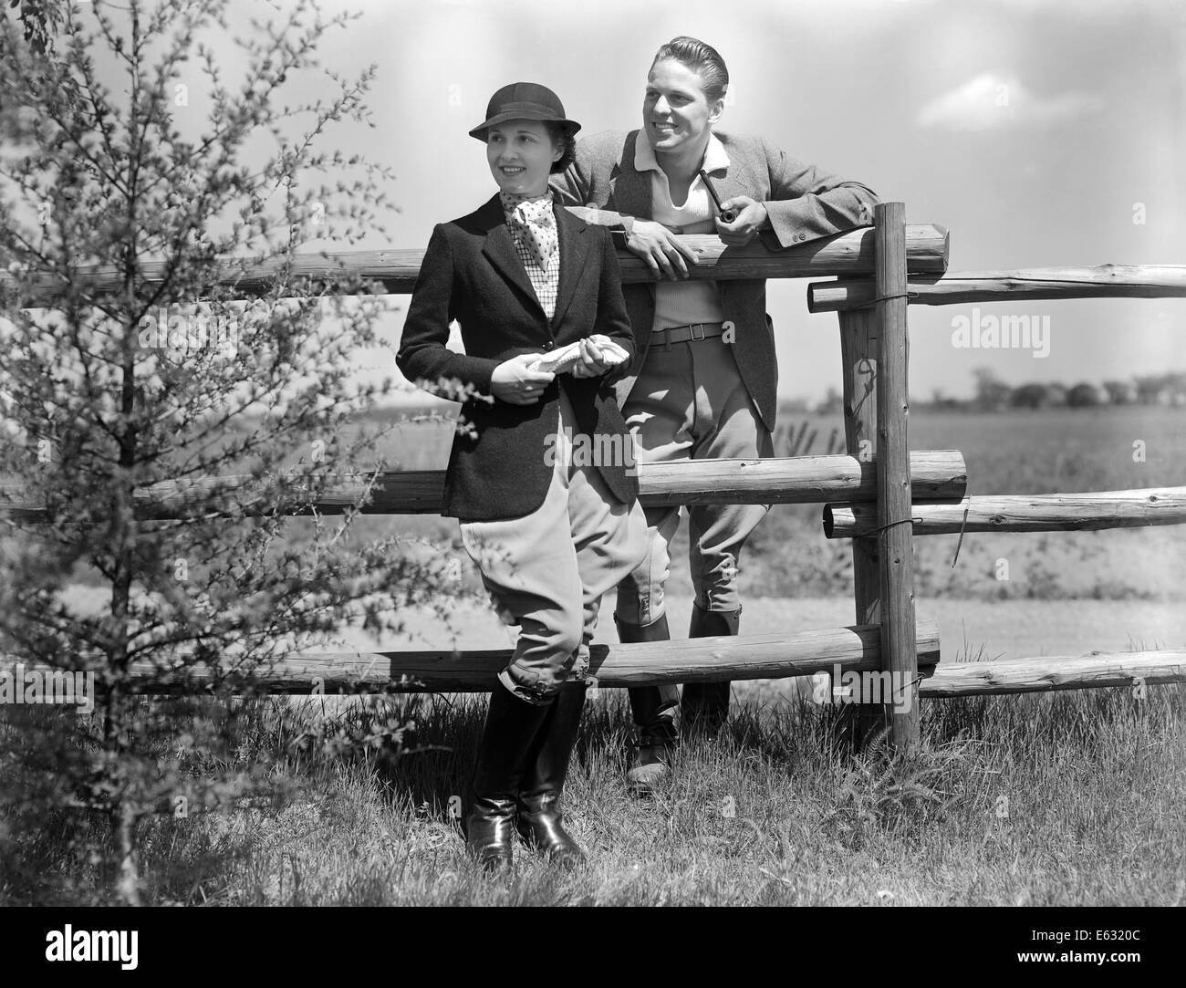 1930 Vêtements d'ÉQUITATION ÉQUITATION COUPLE STANDING TOGETHER PAR RAIL FENCE MAN SMOKING PIPE Banque D'Images