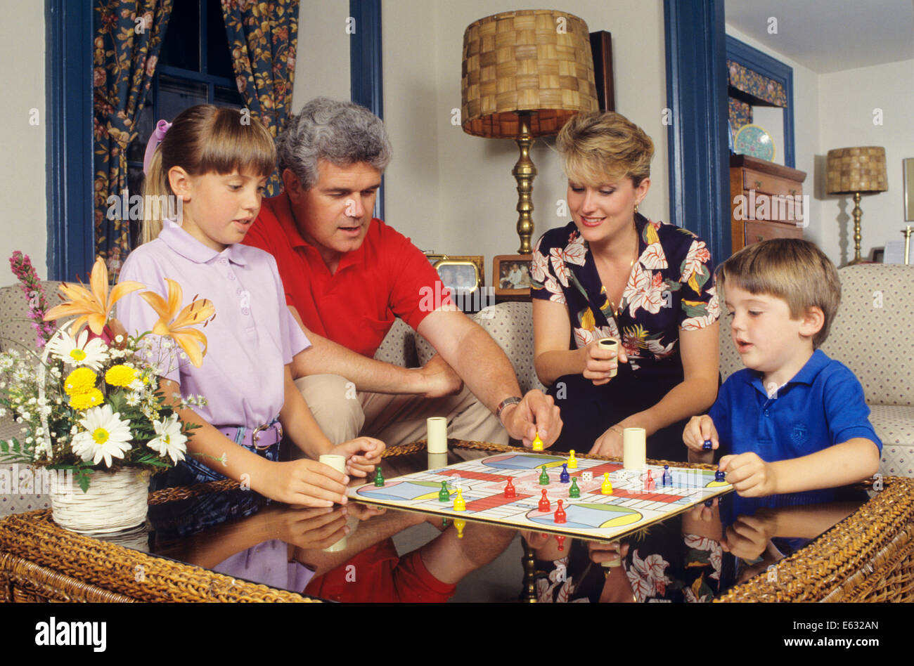 1980s 1990s ENGAGÉ FAMILLE DE QUATRE JOUANT PARCHISI JEU DE SOCIÉTÉ À LA MAISON ASSIS DANS LA SALLE DE SÉJOUR Banque D'Images