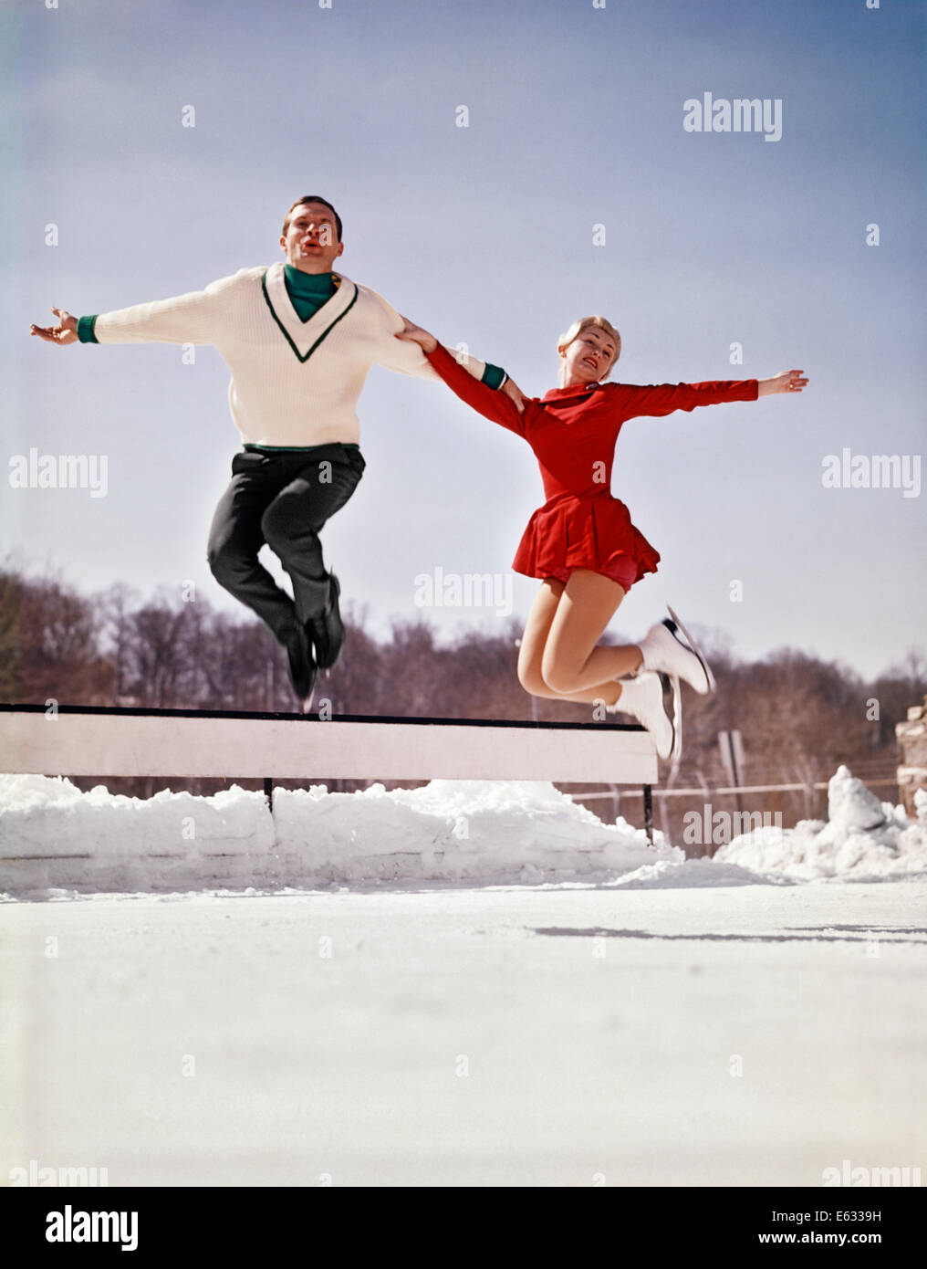 1960 L'HOMME ET LA FEMME PATINEURS sautant en l'air à l'extérieur de la patinoire à la caméra en portant des tenues de patinage Banque D'Images