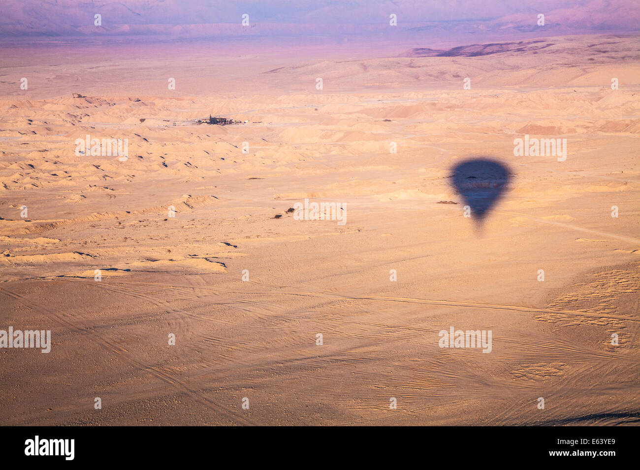 L'ombre d'une montgolfière survolant le désert en Égypte au lever du soleil avec un petit hameau dans la distance. Banque D'Images