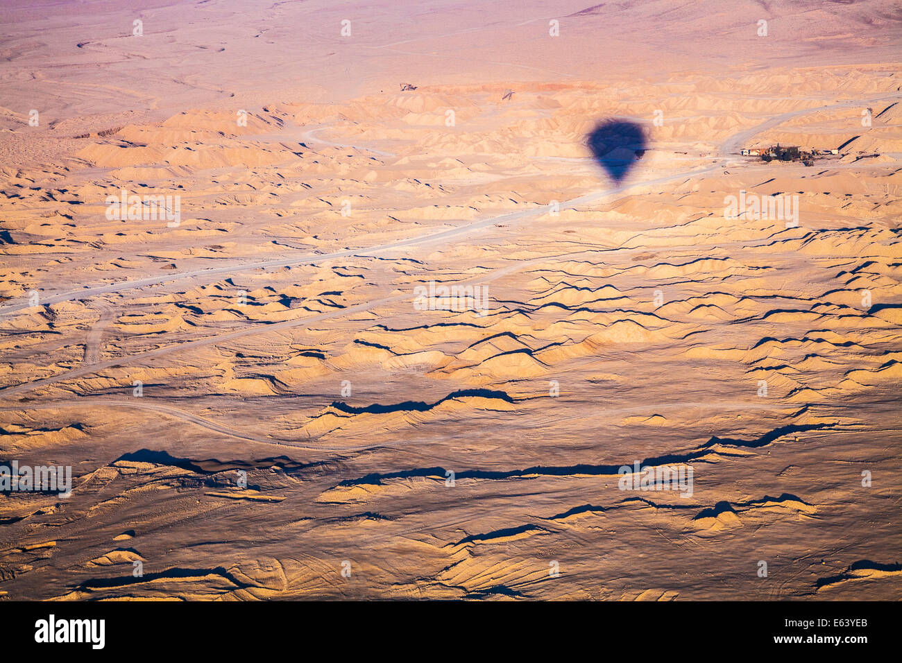 L'ombre d'une montgolfière survolant le désert en Egypte avec un petit hameau dans la distance. Banque D'Images