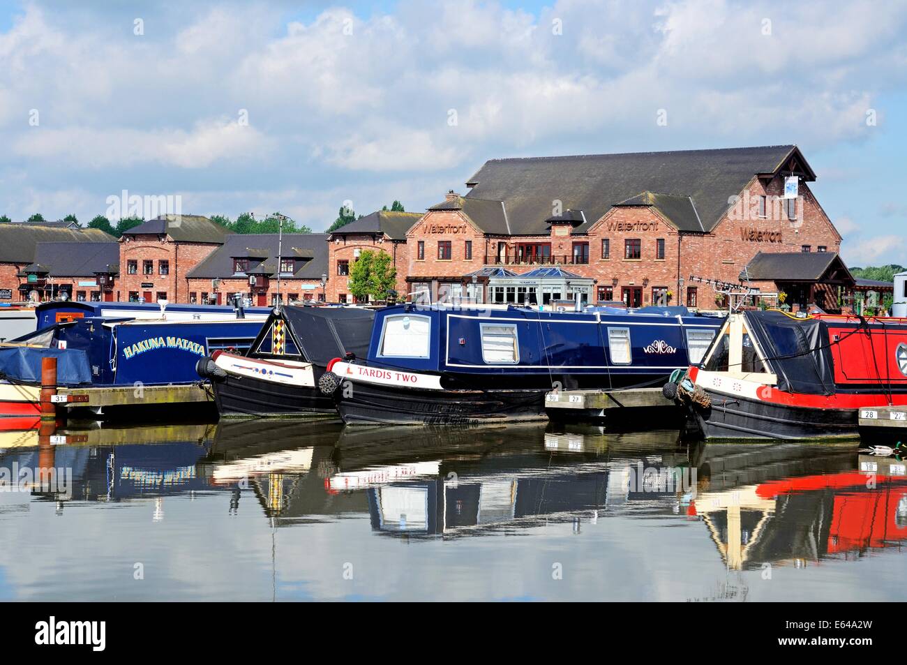 Narrowboats sur leurs amarres dans le bassin du canal, avec des magasins, bars et restaurants à l'arrière, Barton-under-Needwood. Banque D'Images