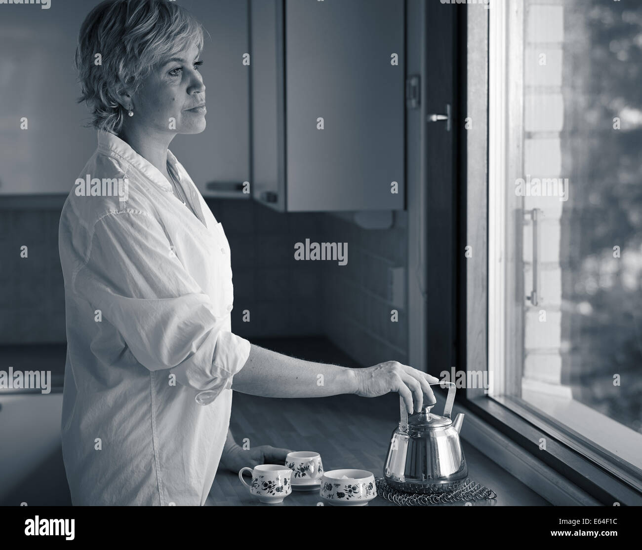 Matin serein moment, mature femme de boire du café dans la cuisine, la lumière du soleil venant de la fenêtre Banque D'Images