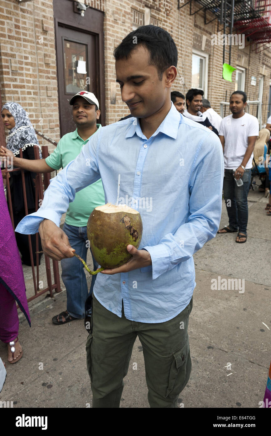 L'homme se prépare à boire le lait d'une noix de coco verte à foire de rue du Bangladesh à Brooklyn à New York, 2014. Banque D'Images