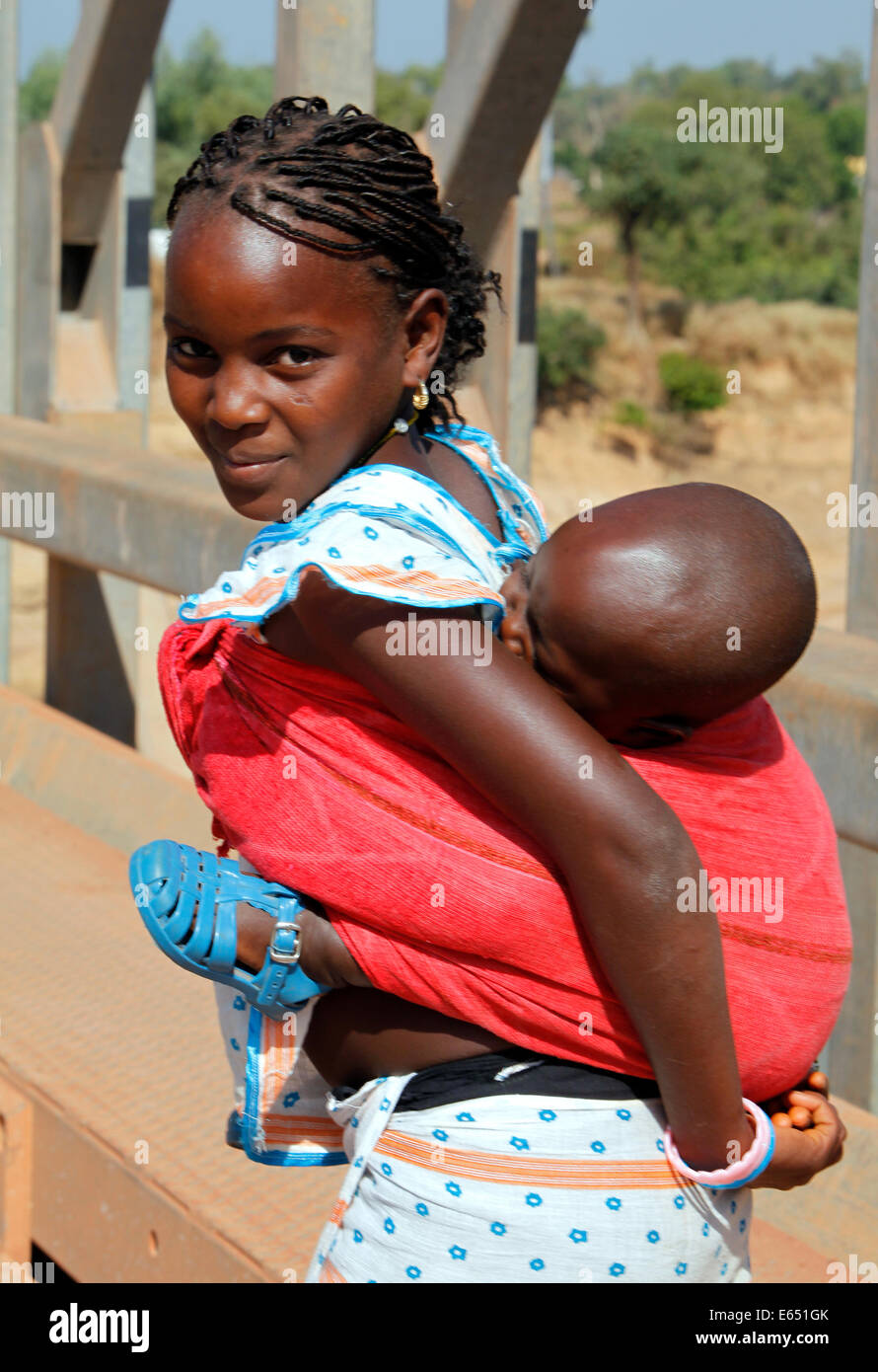 Girl porte sa petite sœur dans un harnais sur son dos, le Sénégal, l'Afrique Banque D'Images