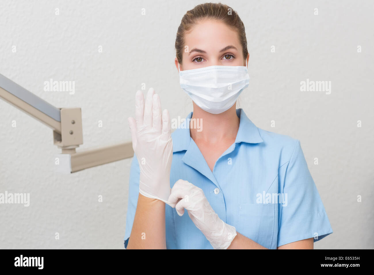 Assistant dentaire en masque à la caméra en tirant sur les gants Banque D'Images