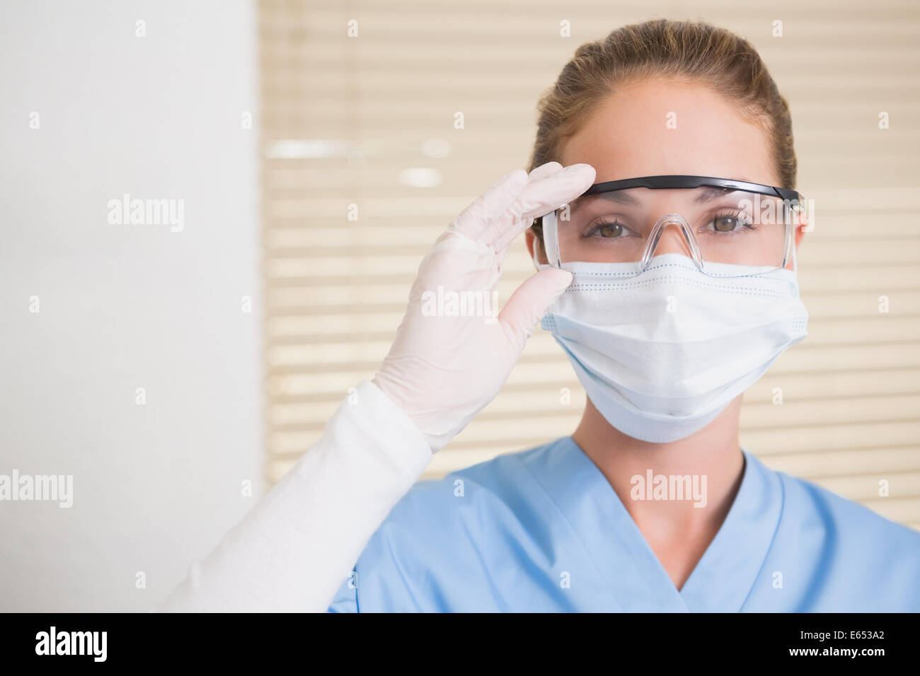 Dentiste dans un masque chirurgical et des lunettes looking at camera Banque D'Images