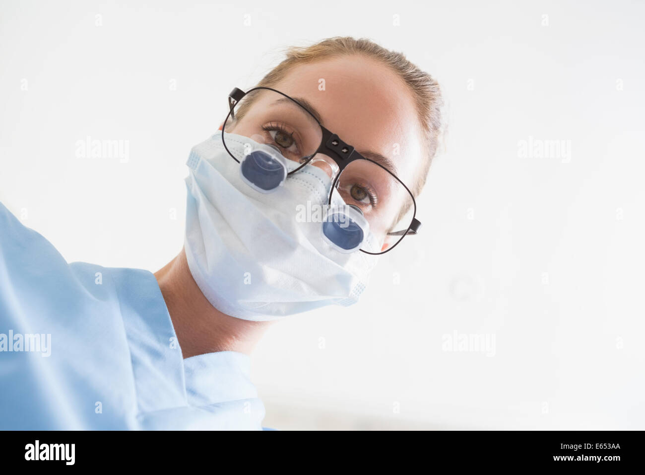 Dentiste en masque chirurgical et dentaire loupes à la recherche vers le bas sur patient Banque D'Images