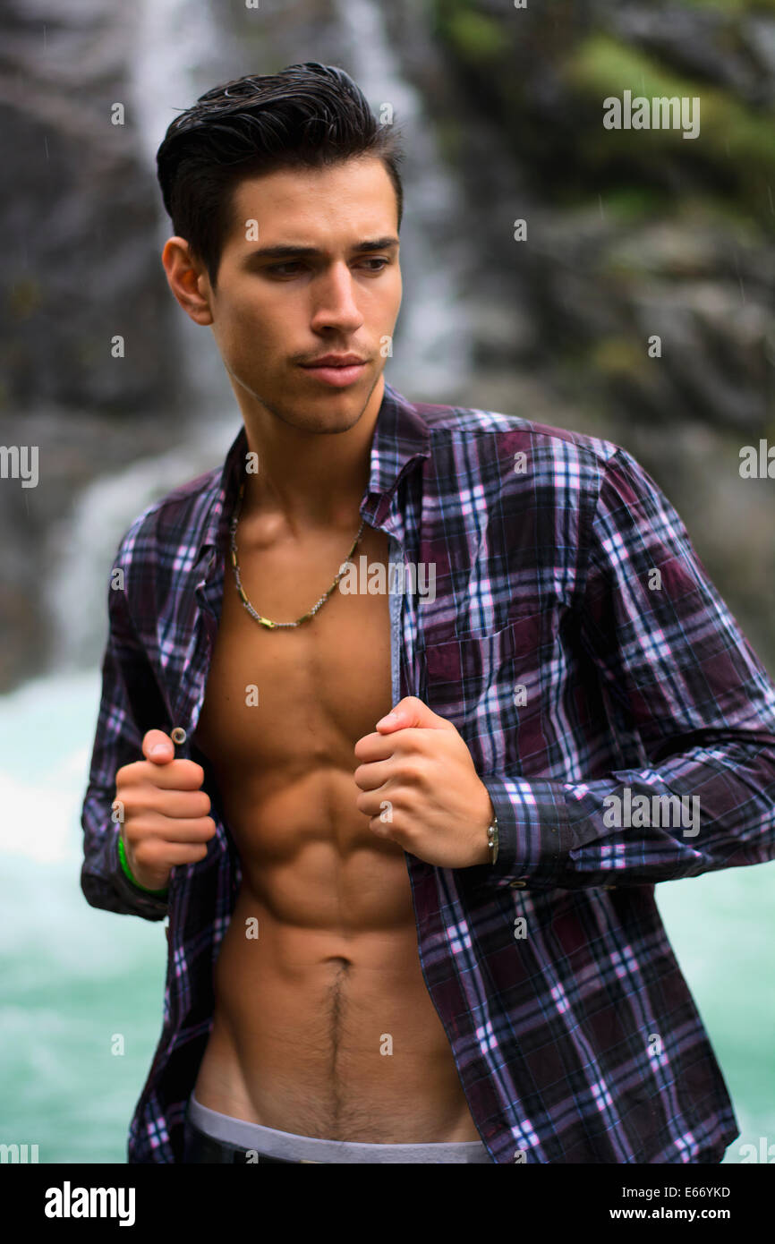 Beau jeune homme près de mountain waterfall avec open shirt déchiré, corps athlétique Banque D'Images