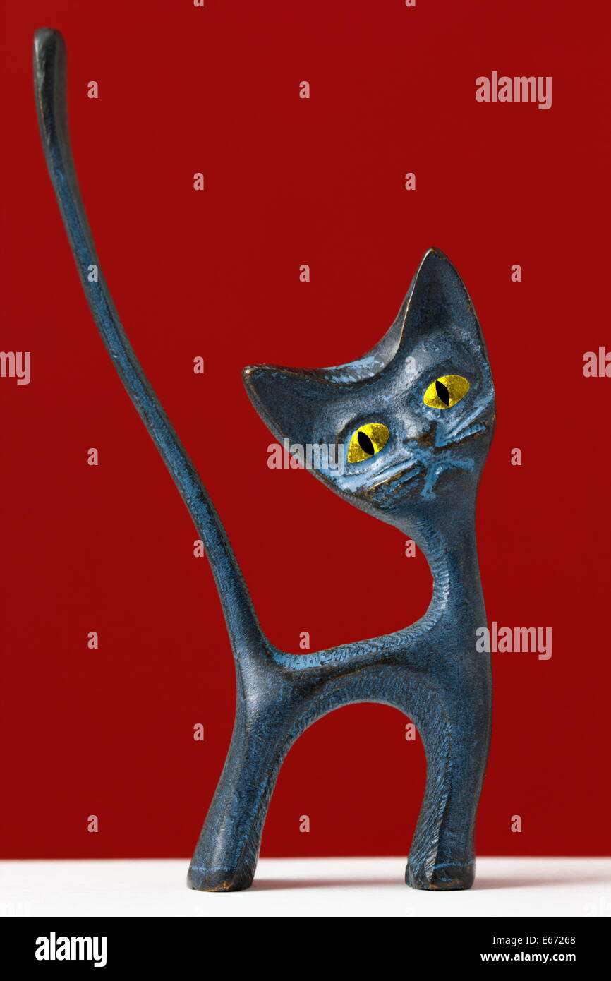 Figurine d'un chat bizarre avec cartoon comme yeux et sa longue queue sur fond rouge. Banque D'Images