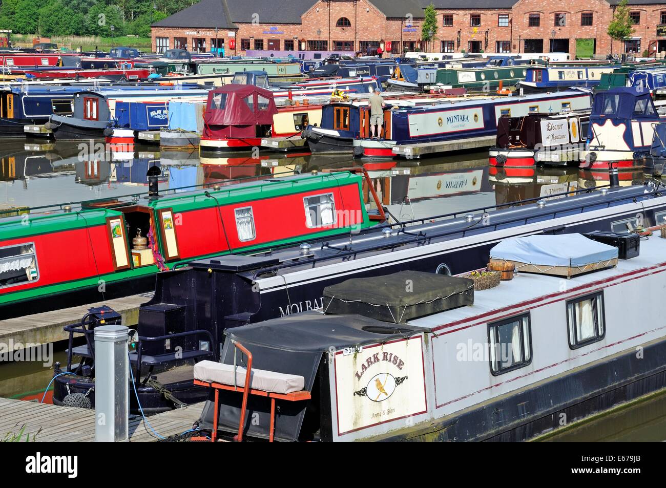 Narrowboats sur leurs amarres dans le bassin du canal avec des bars, boutiques et restaurants à l'arrière, Barton Marina, en Angleterre. Banque D'Images