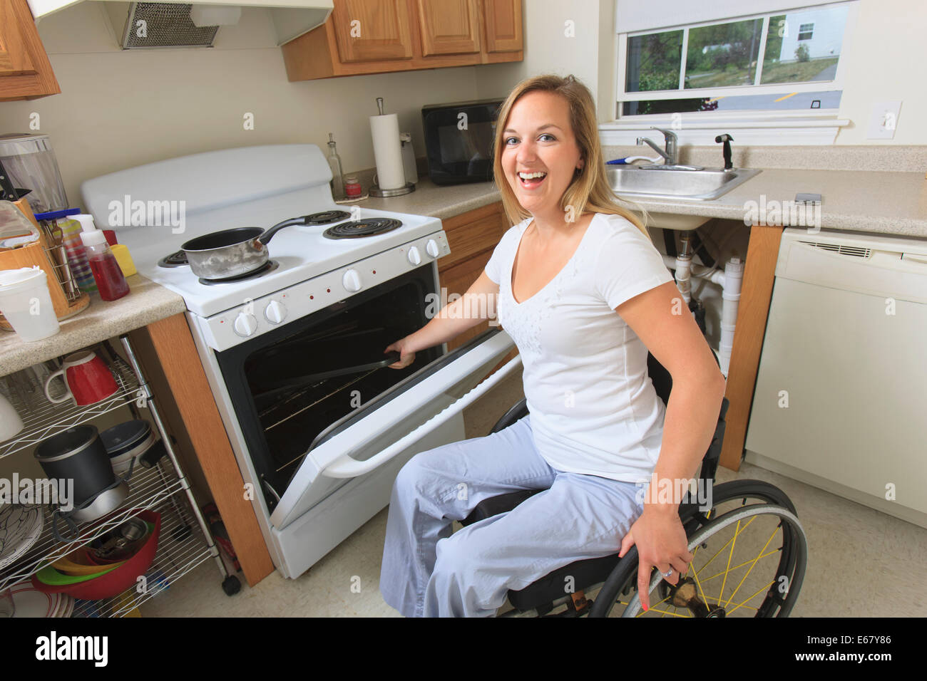 Femme avec de la moelle épinière dans sa cuisine accessible à l'aide d'une cuisinière Banque D'Images