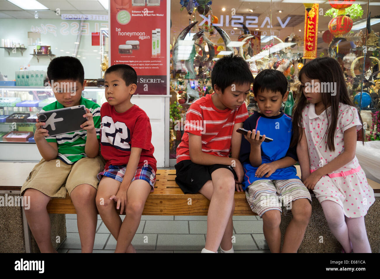 Les enfants asiatiques jeux vidéos sur leurs comprimés dans le jardin d'Asie Mall, Westminster, Orange County, Californie, USA Banque D'Images