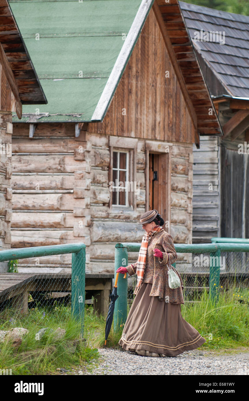 Femme en robe période log cabins and buildings le long de la rue principale de la vieille ville historique de Barkerville ville d'or, British Columbia, Canada. Banque D'Images