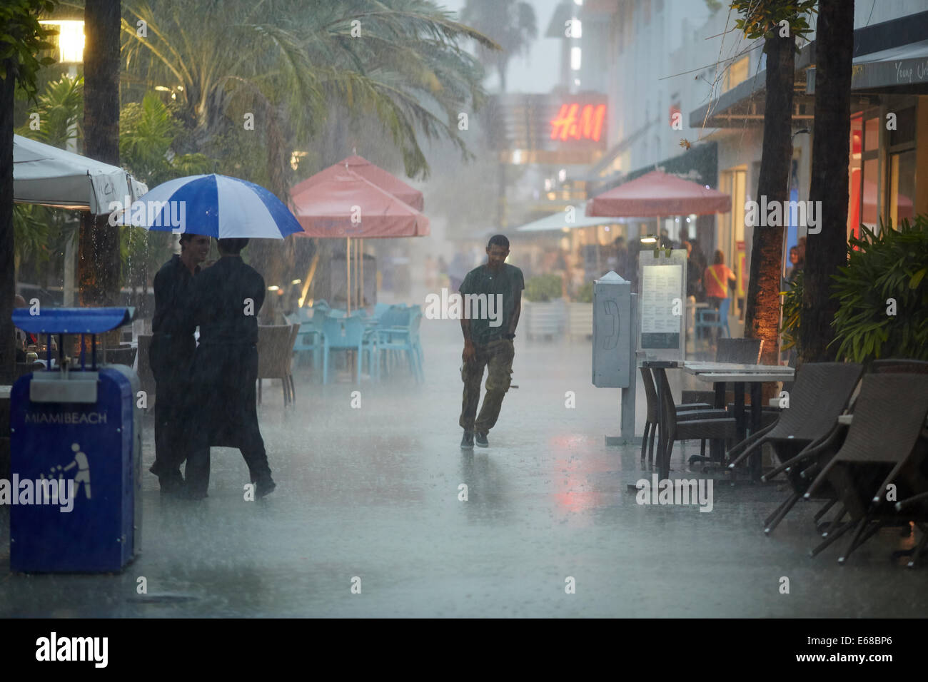 Photo de deux serveurs partageant un parapluie pour servir le public dans la pluie battante Banque D'Images