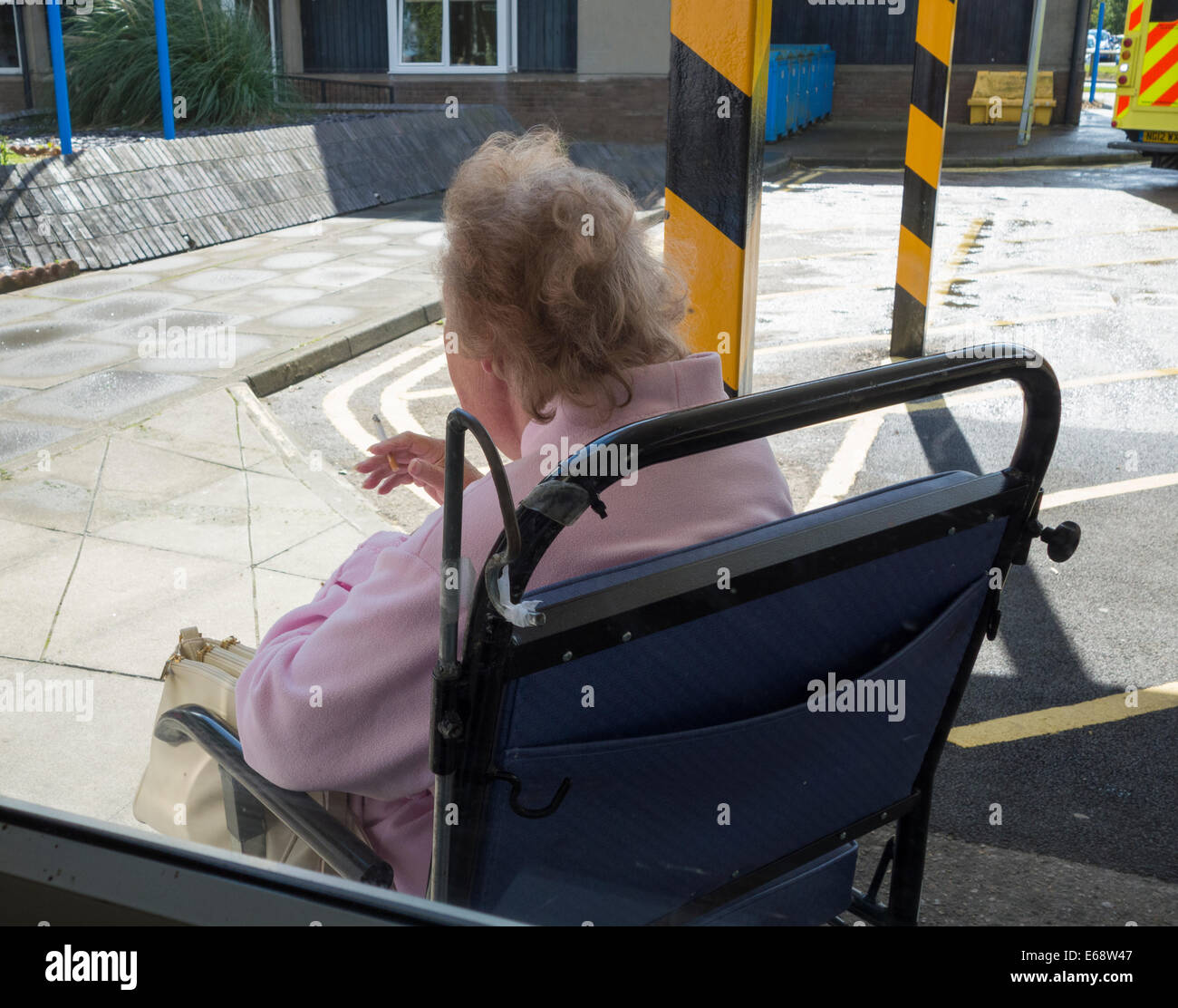 Personnes âgées female patient in hospital wheelchair fumer près de la baie d'ambulance à l'extérieur de l'hôpital NHS, England, UK Banque D'Images