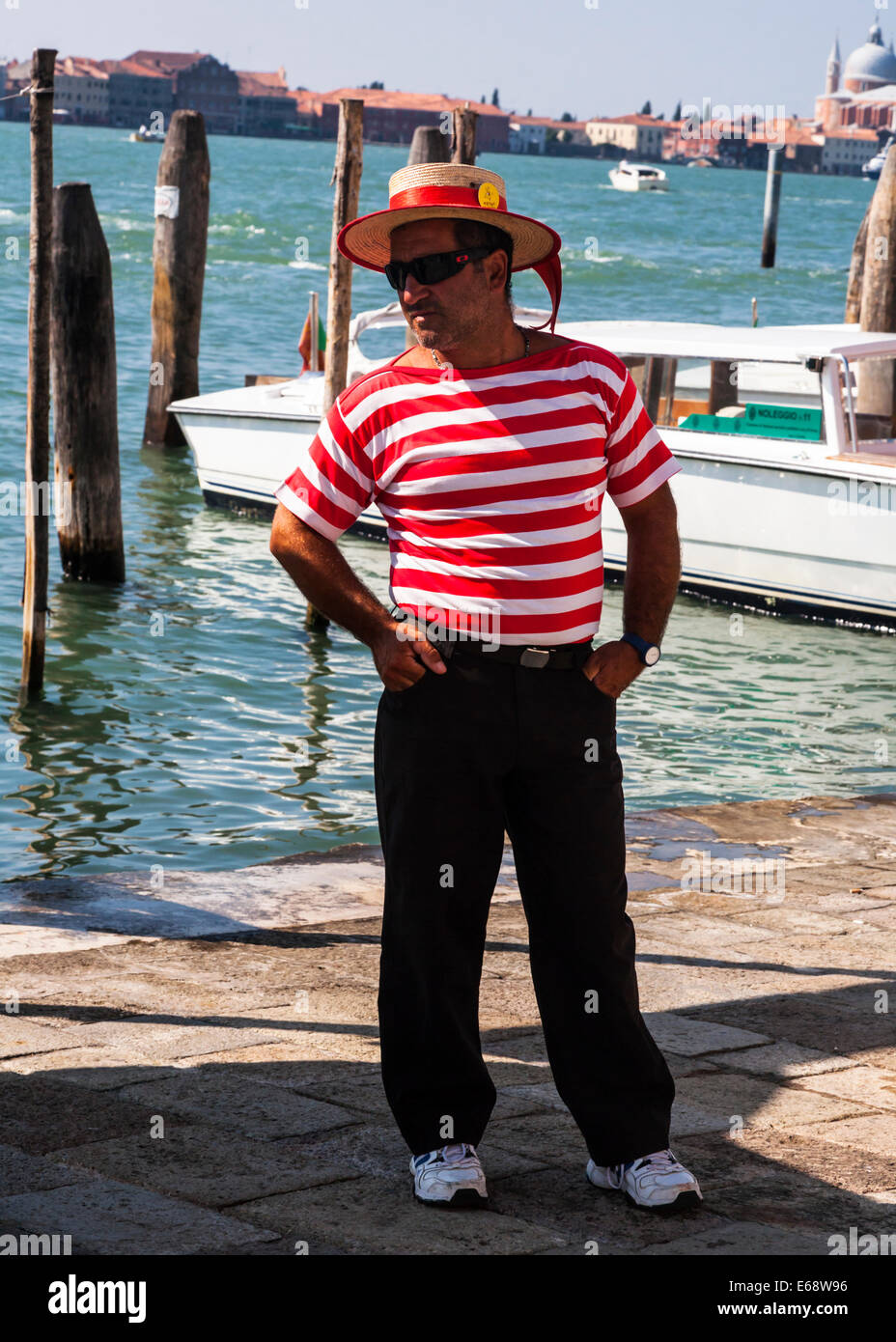 Gondolier debout à bord de l'eau, vêtu du costume traditionnel chemise rayée et chapeau, Venise, Vénétie, Italie. Banque D'Images