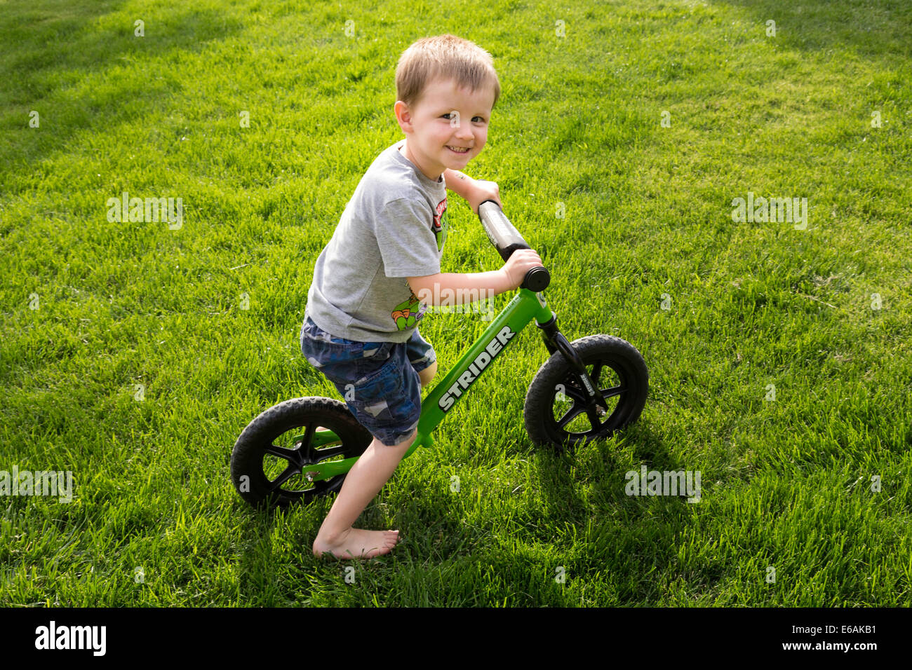Petit Boy Smiling at Camera, assis sur son vélo dans la cour, USA Banque D'Images