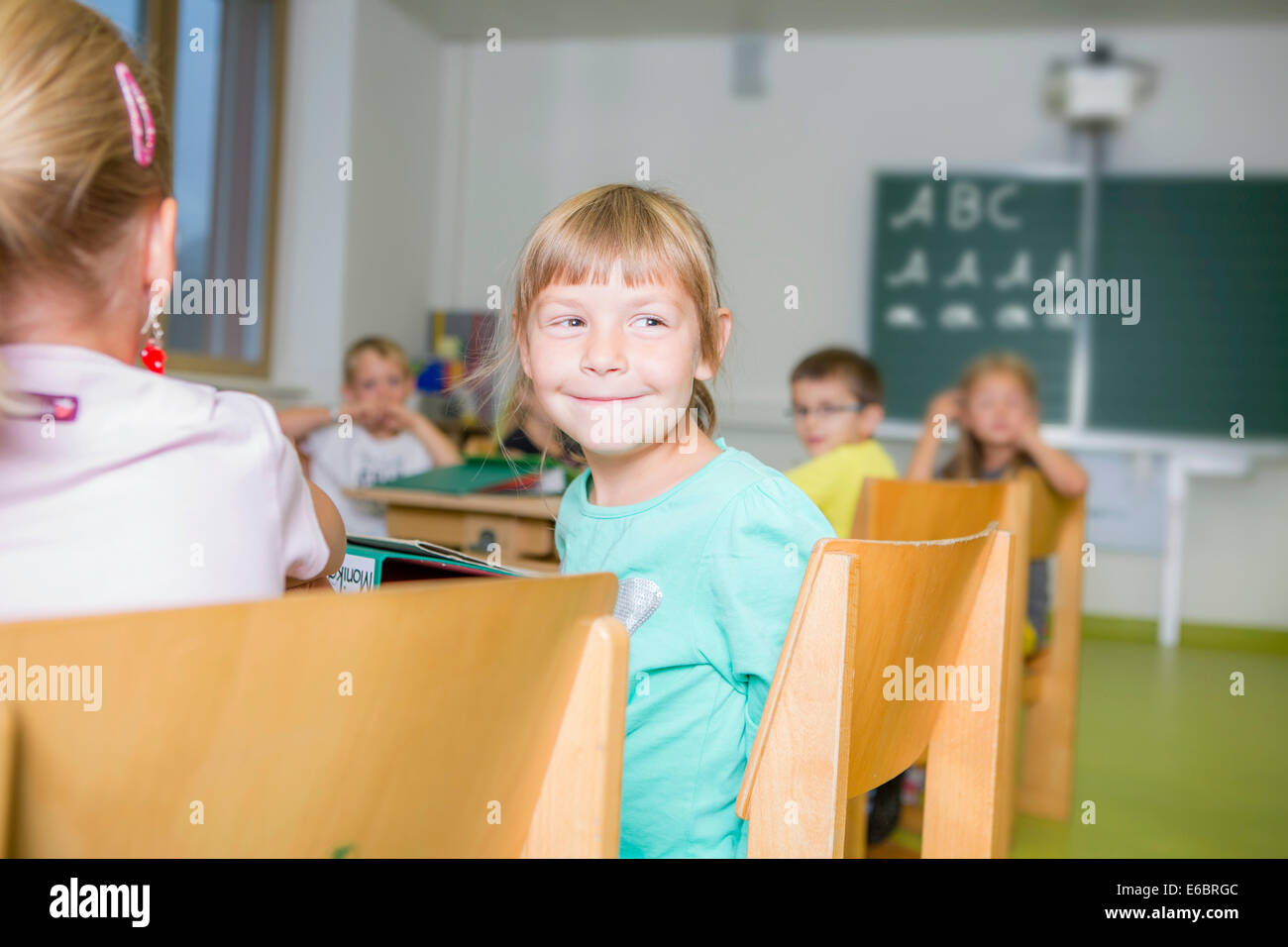Fille, 6, assis à un bureau de l'école et en tournant pour regarder derrière, à Reith im Alpbachtal, district de Kufstein, Tyrol, Autriche Banque D'Images
