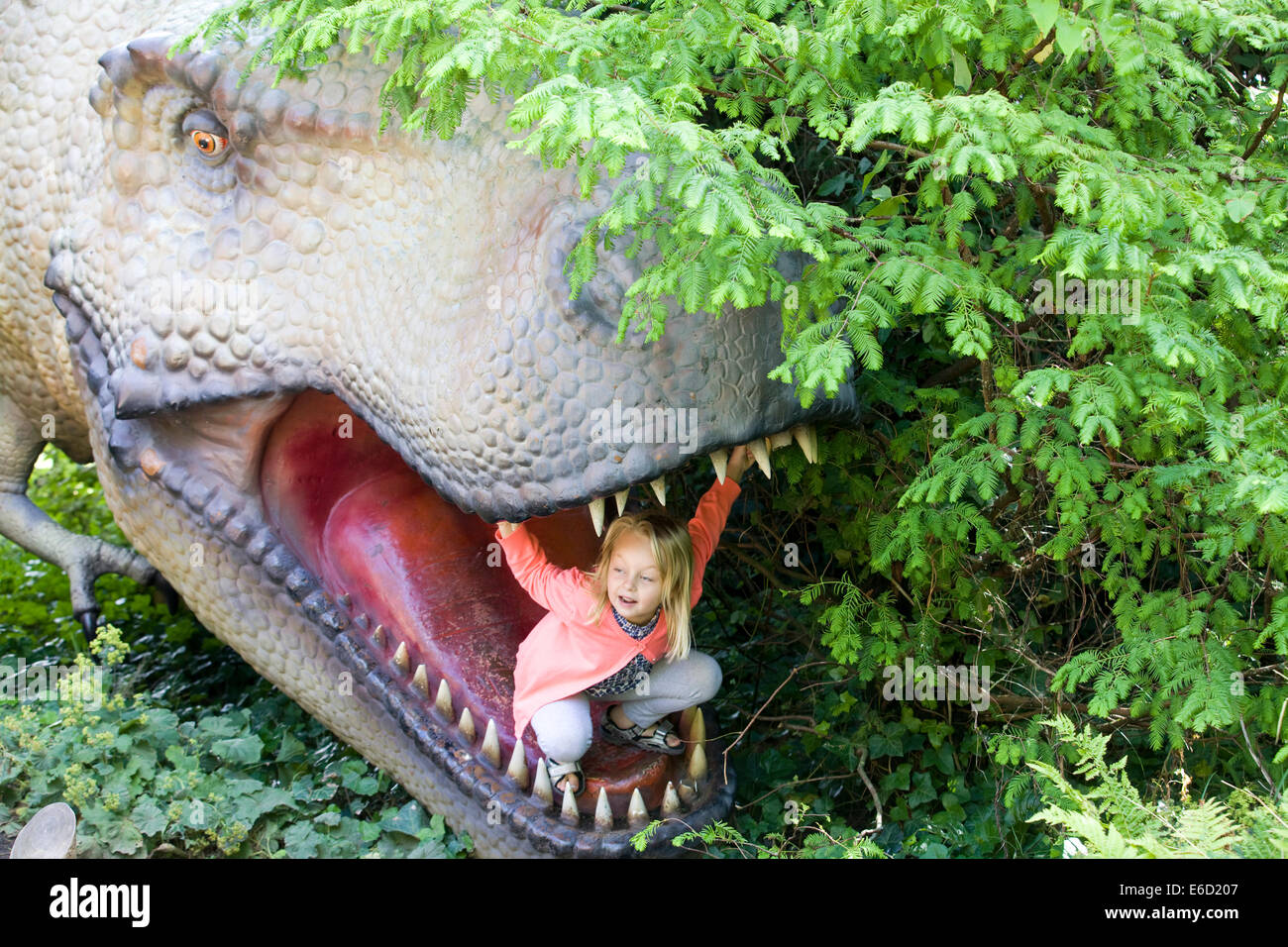 Petite fille à l'intérieur de la bouche d'une statue de dinosaure Banque D'Images