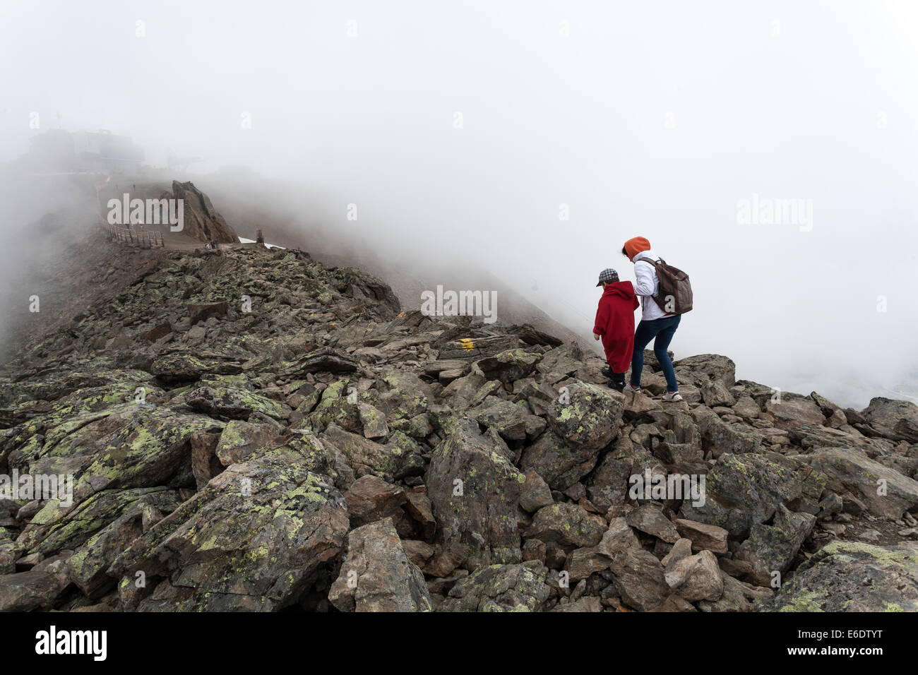 Une femme avec sac à dos et son garçon en rouge sweat longue balade dans le brouillard sur un gros rochers dans les Alpes Banque D'Images