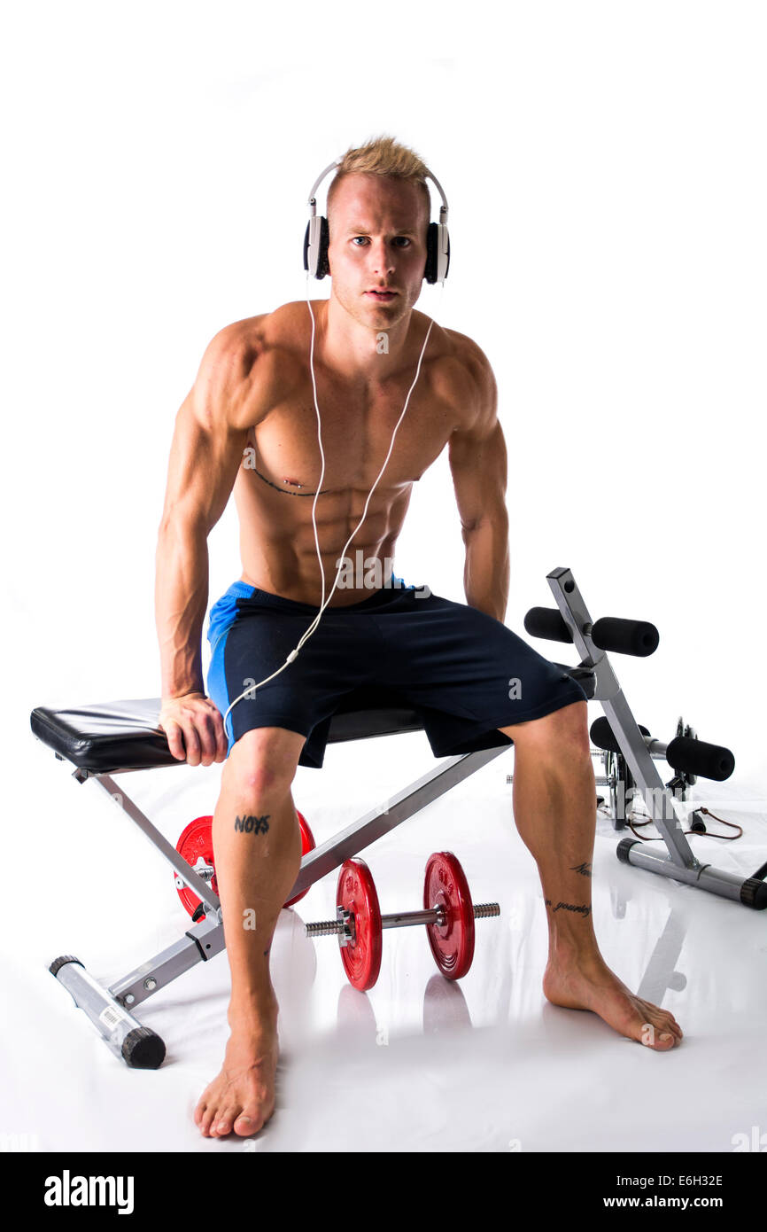 Portrait d'un jeune homme blond musclé soulevant des poids et d'écouter de la musique dans les écouteurs, isolé sur fond blanc Banque D'Images