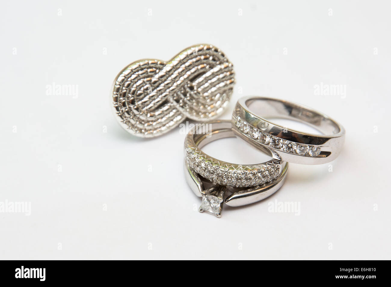 Or blanc et diamants Bandes de mariage une bague de fiançailles sont affichés en face d'un symbole de l'infini d'argent. Banque D'Images Or blanc et diamants Bandes de mariage une bague de fiançailles sont affichés en face d'un symbole de l'infini d'argent. Banque D'Images