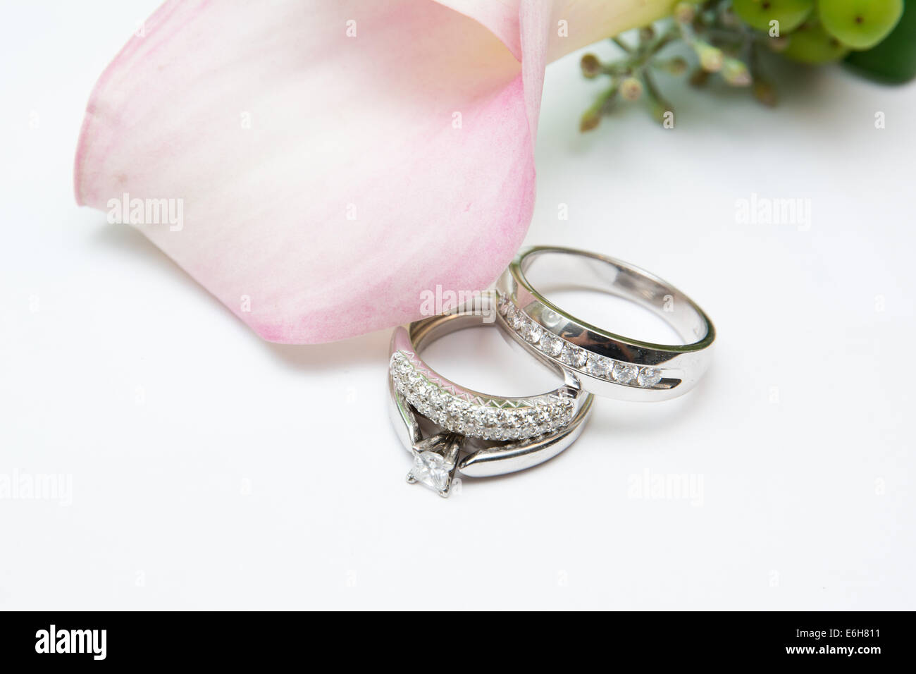 Or blanc et diamants de mariage et une bague de fiançailles sont affichés sur un fond blanc à côté des fleurs de mariage rose. Banque D'Images