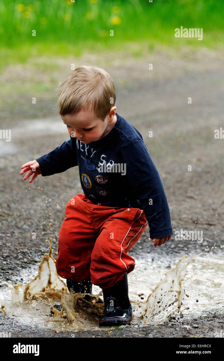 Un jeune garçon se tremper en marche dans une flaque d'eau Banque D'Images