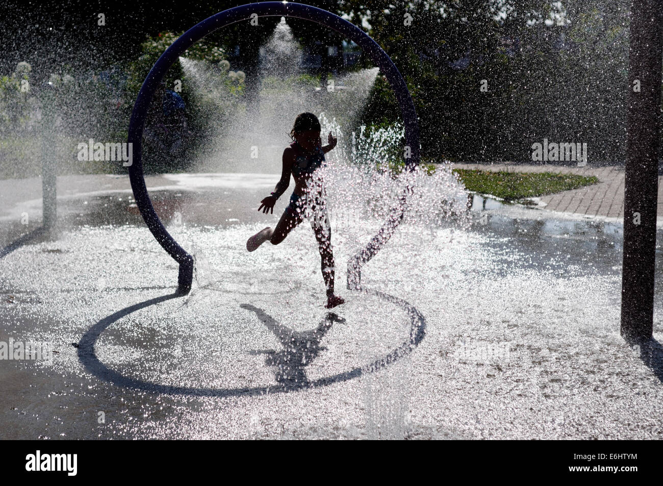 Une jeune fille jouant dans les fontaines d'eau sur une chaude journée d'été Banque D'Images