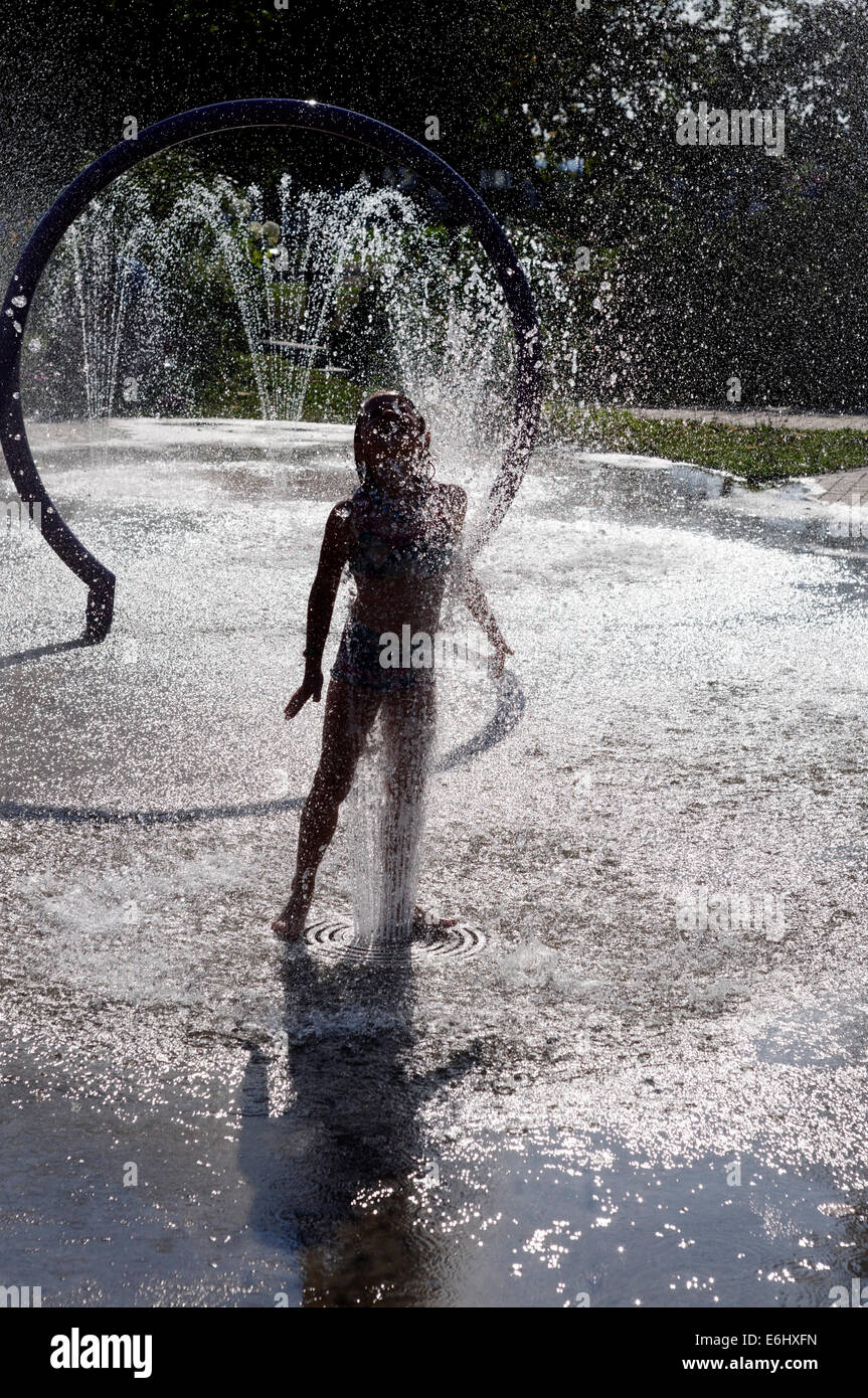 Une jeune fille jouant dans les fontaines d'eau sur une chaude journée d'été Banque D'Images