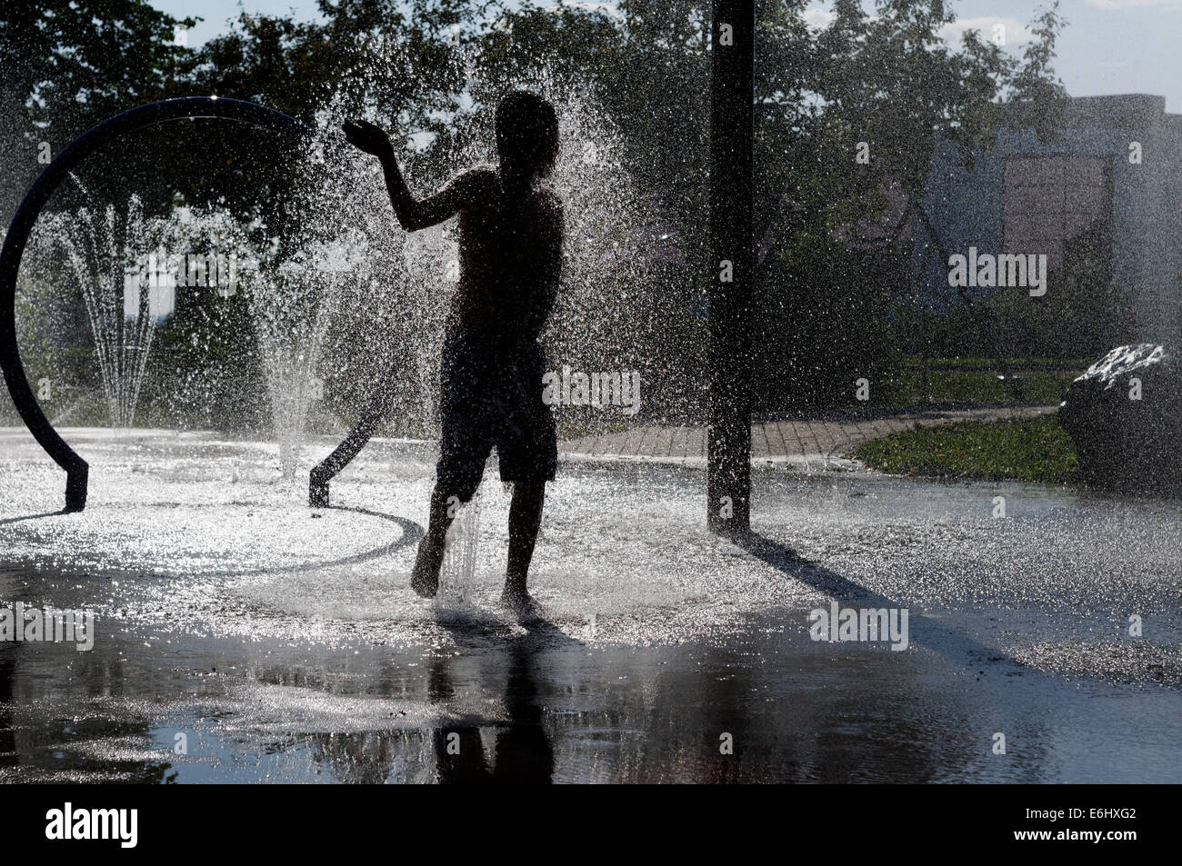 Un jeune garçon jouant dans les fontaines d'eau sur une chaude journée d'été Banque D'Images