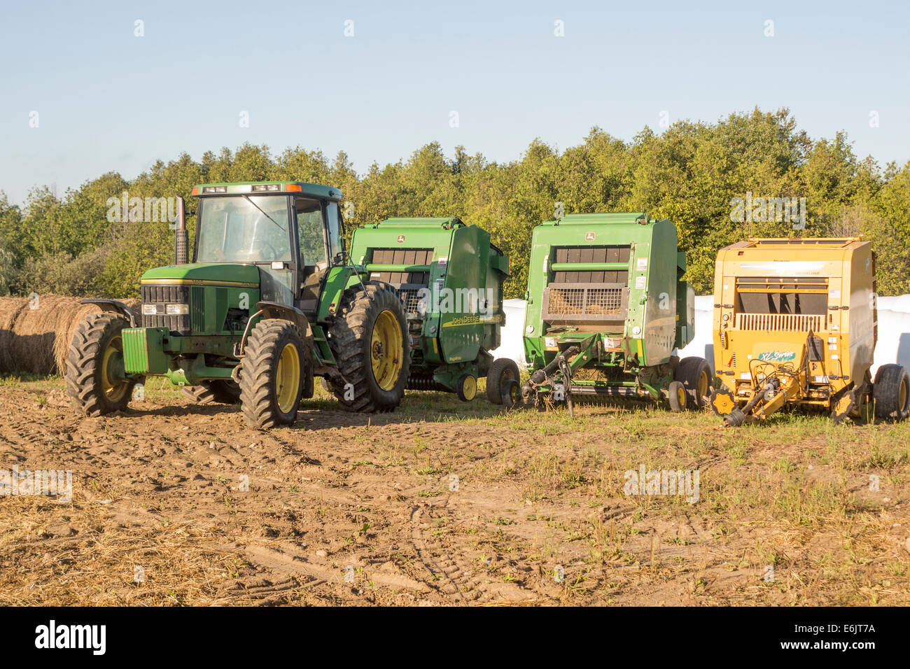 John Deere 7400 Tracteur avec presse à balles de foin rondes attachées à l'avant d'une rangée de balles rondes couvertes de plastique. Banque D'Images