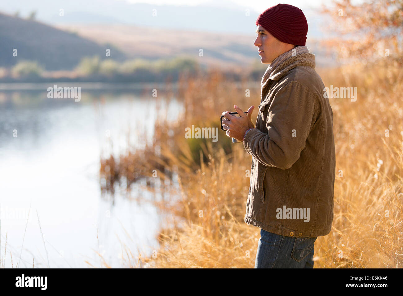 Thoughtful man standing by Lake et de boire du café à l'automne Banque D'Images Thoughtful man standing by Lake et de boire du café à l'automne Banque D'Images