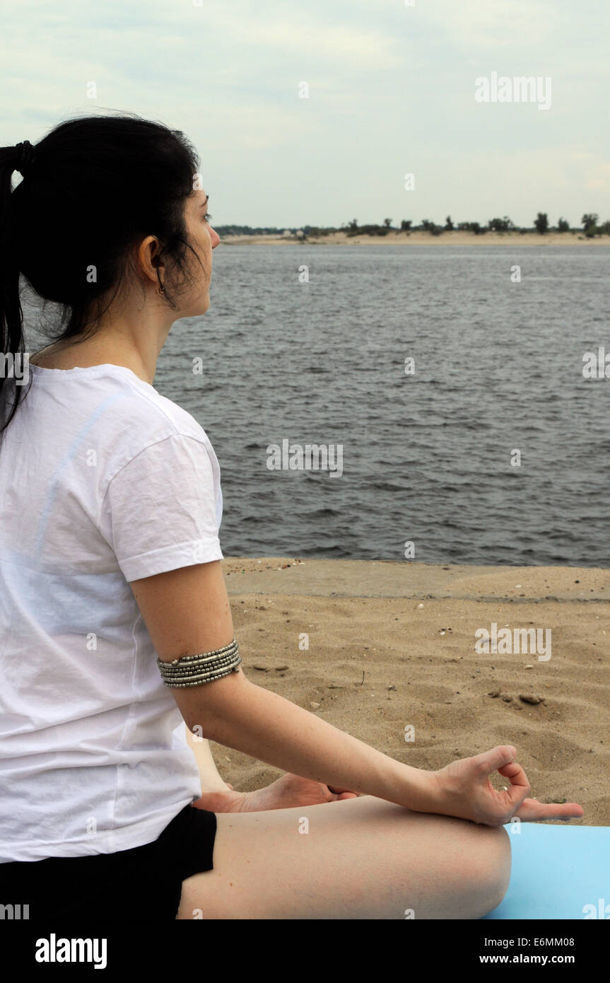Femme assise en position du lotus, à la recherche au niveau de la rivière Banque D'Images