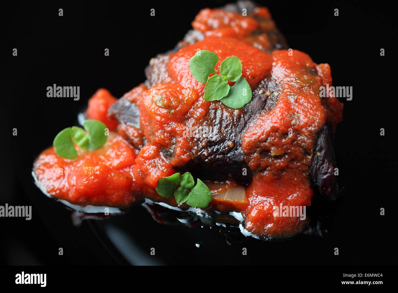 Rôti de boeuf avec sauce tomate et basilic. Focus sélectif. Fond noir. Close-up. Banque D'Images