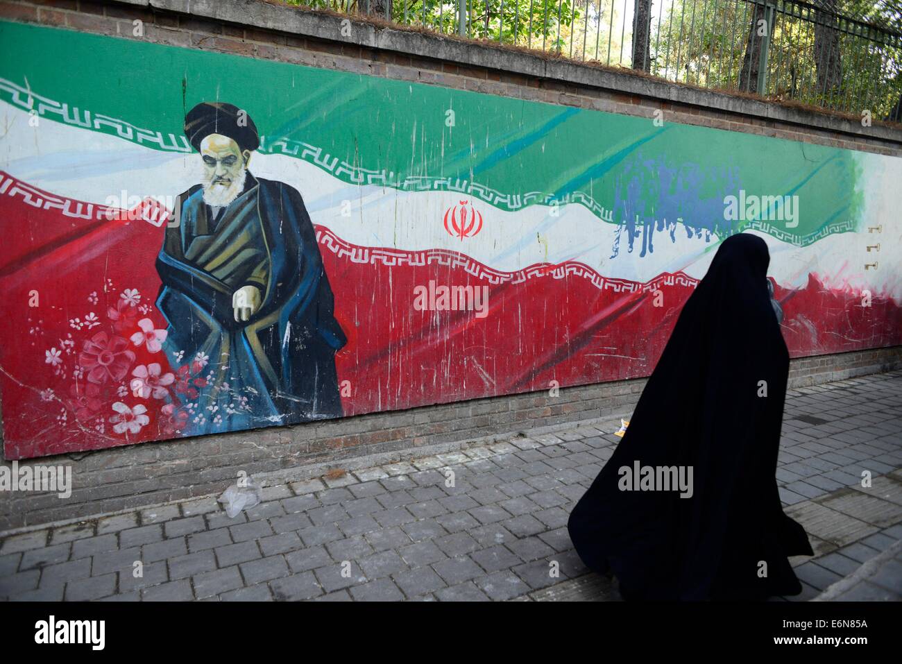 Femme iranienne voilée, promenades au-delà d'un Ayatollah Khomeini's photo peint sur un mur de l'ancienne ambassade des États-Unis à Téhéran, Iran. Banque D'Images