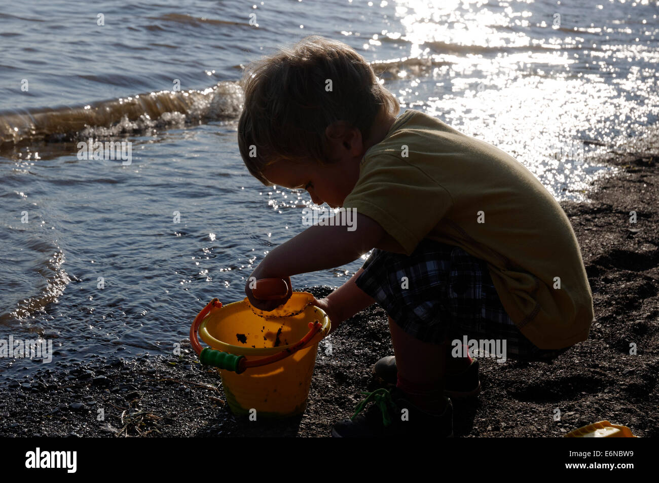 Un jeune garçon jouant avec un seau et la cosse sur la plage Banque D'Images